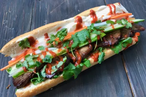 En saftig banh mi med tofu, färska grönsaker och en härlig sås på en träbakgrund.