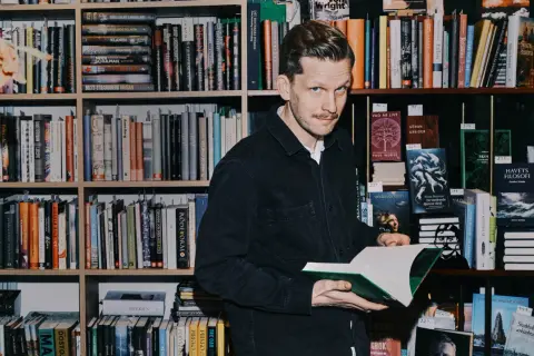 Robin Olovsson står bland bokhyllor och håller en öppen bok.