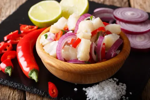 Pyszne ceviche z kawałkami ryby, czerwoną cebulą, papryką i chili, podane z limonką i solą.