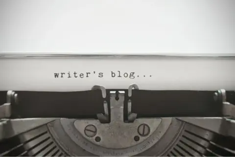Maszyna do pisania z napisem "writer's blog...". Zastanawiasz się, jak napisać bloga po angielsku? Zacznij od tego!