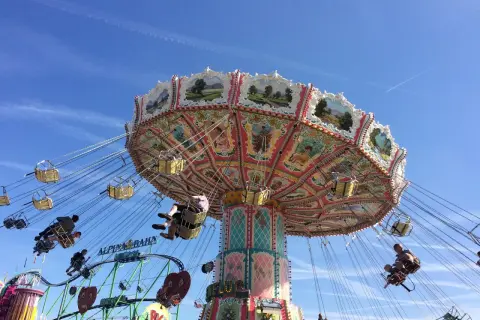 Carrusel giratorio en un oktoberfest parque de atracciones, con gente disfrutando del paseo bajo un cielo azul.