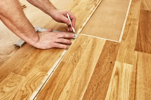 Un bricoleur utilise une règle et un crayon pour marquer une ligne de coupe sur du parquet flottant, étape essentielle pour savoir comment couper du parquet flottant.