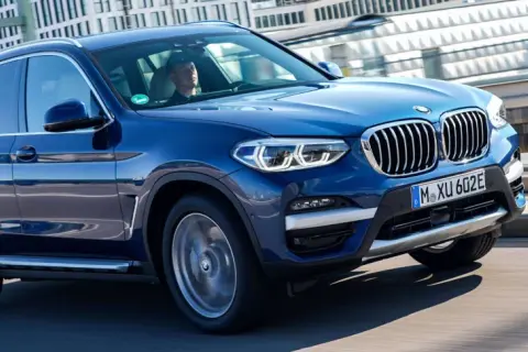 Niebieskie BMW X3 w ruchu miejskim. Zastanawiasz się, ile kosztuje BMW X3? Ten model wygląda na nowy i luksusowy.