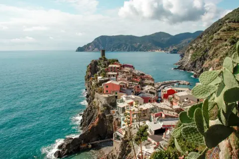 Pueblo costero de casas coloridas en un acantilado, con el mar azul y montañas al fondo. Un lugar que evoca la esencia de la spezia el ejido.