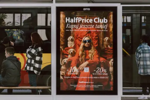 Plakat reklamuje HalfPrice Club, zachęcając do zakupów z rabatami. Aplikacja HalfPrice to szansa na niższe ceny.