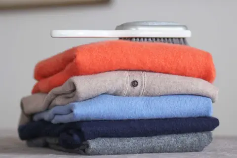 Ein Stapel bunter Kaschmirpullover, bereit für die Pflege. Was ist Kaschmir? Weiche Wolle für luxuriöse Kleidung.