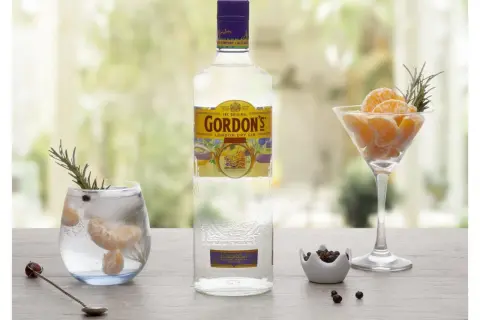 Gordon's alkohol: butelka ginu, drink z mandarynką i rozmarynem, kieliszek z mandarynką i rozmarynem, miseczka z jałowcem.
