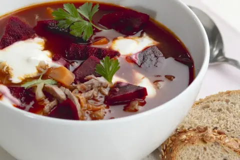Herzhaftes Borschtsch-Rezept: Rote Bete, Fleisch und ein Klecks Sahne in einer Schüssel, dazu Brot.
