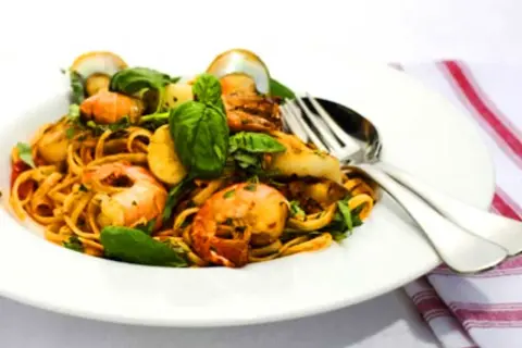 En tallrik med linguine frutti di mare, toppad med färska örter och serverad med bestick.