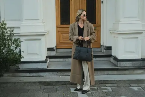En kvinna med solglasögon bär en elegant brun kappa och håller en stilren vero moda väska.