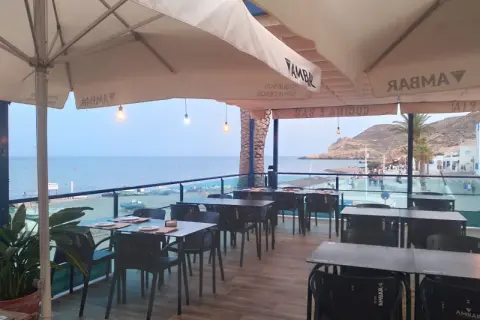 Terraza de restaurante con mesas y sillas, vistas al mar y a la playa. Un lugar ideal para disfrutar de un socorrito las negras al atardecer.