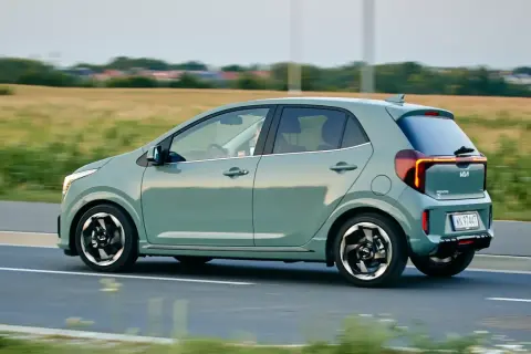 Zielony Kia Picanto w ruchu drogowym, widok z boku, z polem w tle.
