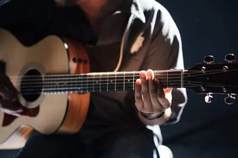 Person übt das Spielen einer akustik gitarre. Hände formen Akkorde auf dem Griffbrett, während die andere Hand die Saiten anschlägt.