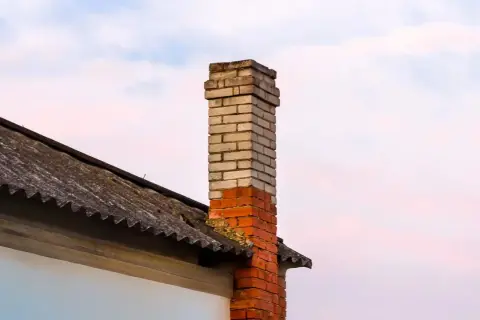 Mokry komin na strychu, z cegły, częściowo zniszczony, na tle nieba.