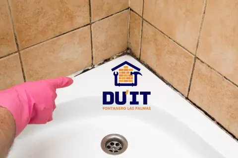 Mano con guante rosa señalando moho en juntas de baño. ¿Cómo sellar un baño? DU'IT Fontanero Las Palmas.