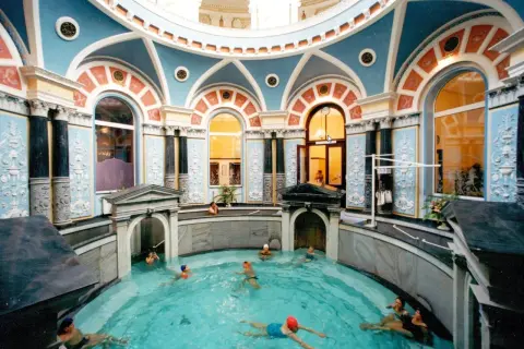Wnętrze z basenem, gdzie ludzie relaksują się w gorącym źródle. Architektura z błękitnymi i pomarańczowymi zdobieniami.