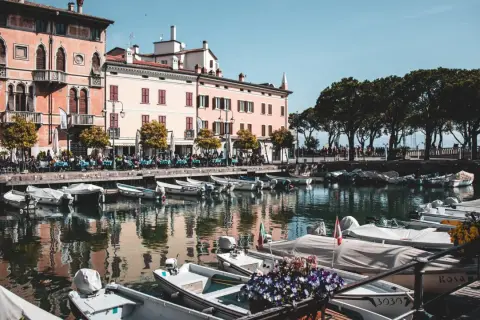 Barche ormeggiate nel porto di Desenzano del Garda, con edifici colorati e alberi sullo sfondo.