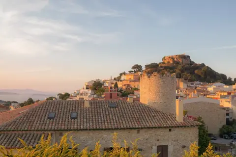 Sonnenuntergang über einem Dorf an der Girona Costa Brava. Ein alter Turm und ein Schloss auf einem Hügel über weiß getünchten Häusern.