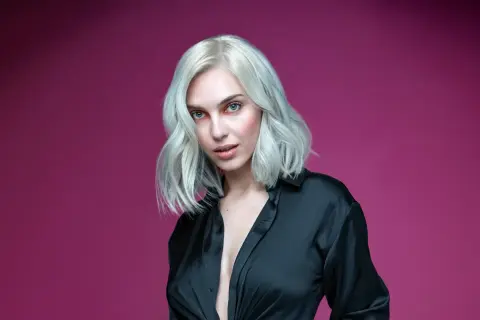 Mujer con cabello rubio platino y ojos azules, vestida con una camisa negra. Aprende como matizar el pelo en casa para lograr este look.