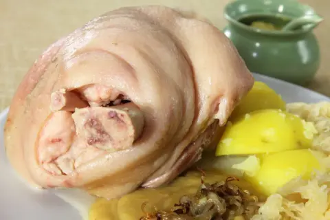 Ein deftiges, gekochtes Eisbein mit Salzkartoffeln, Sauerkraut und einer kleinen Schale mit Soße.