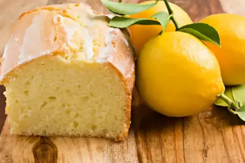 Un délicieux moelleux au citron, avec un glaçage blanc et des citrons frais sur une planche en bois.