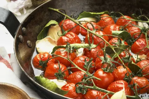 Saftige cherry tomaten mit Knoblauch und Lorbeerblättern in einer Pfanne, bereit zum Garen.