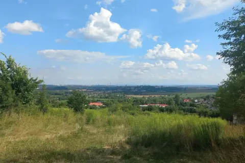 Widok z góry św. Doroty na zieloną dolinę z domami i miastem w oddali. Błękitne niebo z białymi chmurami.