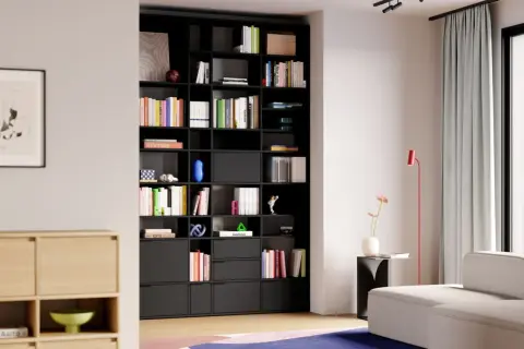 Moderne studio einrichtung mit schwarzem Regal voller Bücher und Deko-Objekte. Ein helles Sofa und ein roter Stehlampen ergänzen den Raum.