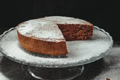 Torta al cioccolato soffice, una delizia senza farina e lievito, cosparsa di zucchero a velo su un'alzata di vetro.