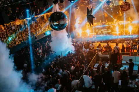 Multitud bailando en una discoteca con luces de neón, humo y una bola de discoteca, celebrando la nochevieja en Zaragoza.