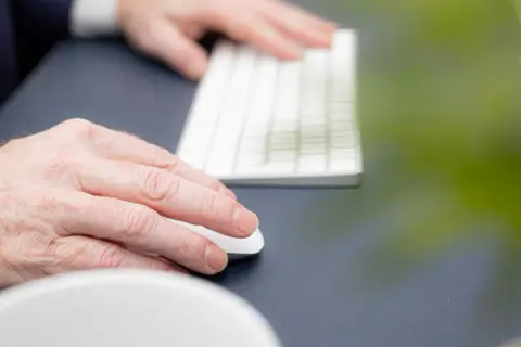 Händer som arbetar vid ett tangentbord och en mus. En person upplever en kramp i armen efter långvarigt arbete.