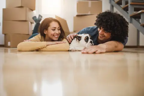 A happy couple and their bulldog relax on the floor amidst moving boxes, ready for their new home.