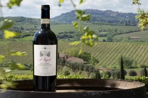 Bottiglia di vino nobile di Montepulciano DOCG su un barile, con vigneti e colline toscane sullo sfondo.