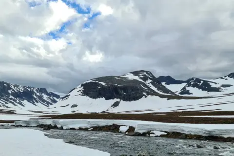 Snöklädda berg och en forsande älv i Jämtland, en vy som inspirerar till att bestiga Sylarna.