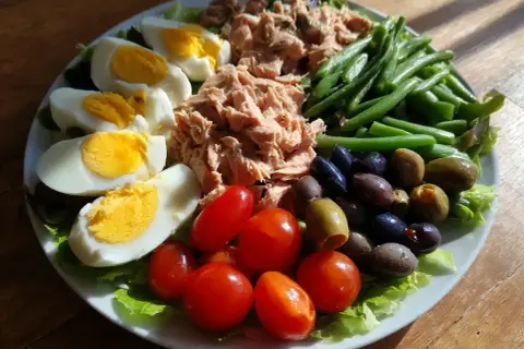 En härlig sallad nicoise med ägg, tonfisk, gröna bönor, tomater och oliver på en bädd av sallad.