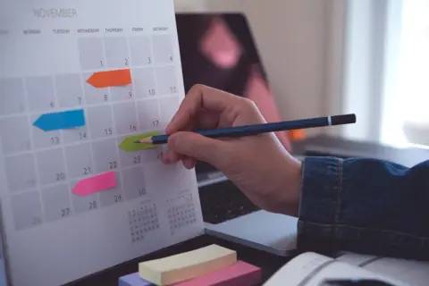 Kalender med färgglada post-it-lappar markerar viktiga datum. En hand med en penna planerar för bokslut enskild firma.