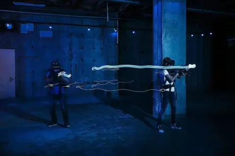 Två personer spelar VR-spel med ljusgevär i en mörk lokal. Perfekt för inomhusaktiviteter i Stockholm.