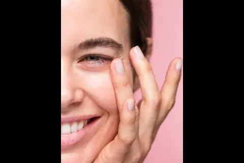 Una mujer sonríe mientras se aplica suavemente un producto en el contorno de ojos. Las opiniones sobre contorno ojos freshly son muy positivas.