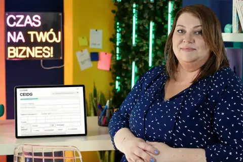 Kobieta w biurze, obok tablet z formularzem CEIDG. Neonowy napis "Czas na Twój Biznes!" sugeruje tematykę zakładania działalności i prawo spółek handlowych.