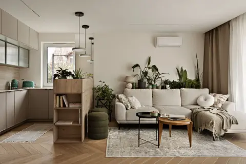 Jasna kuchnia z salonem, z zielonymi akcentami i mnóstwem roślin. Sofa w salonie, stoliki kawowe i regał z książkami.