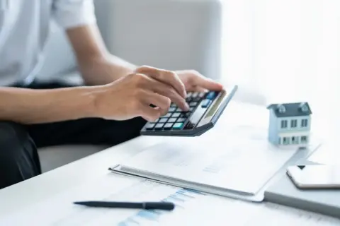 Man calculando la viabilidad hipoteca con calculadora, papeles y maqueta de casa.