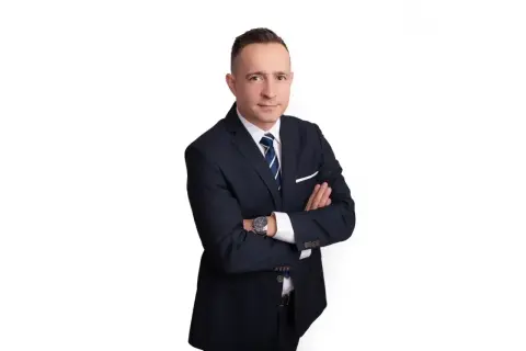 Mężczyzna w garniturze ze skrzyżowanymi rękami, na białym tle.