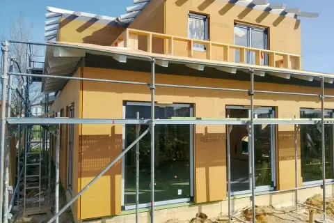 Casa en construcción con paredes exteriores prefabricadas de madera, andamios y cielo azul.