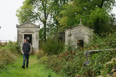 Un homme marche dans un cimetière abandonné en France, entouré de mausolées envahis par la végétation.