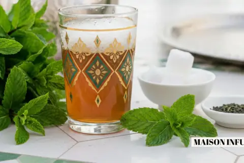 Un verre de thé à la menthe fraîche, orné de motifs dorés et verts, est prêt à être dégusté avec des morceaux de sucre et des feuilles de thé.