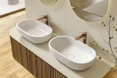 Due lavabi ovali bianchi su un mobile bagno su misura con finitura a listelli verticali. Rubinetteria color rame.