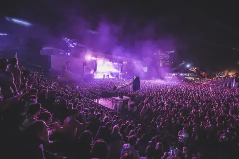 Tłum ludzi na nocnym koncercie, fioletowe światła i dym tworzą magiczną atmosferę. To niezapomniane u2 koncerty.