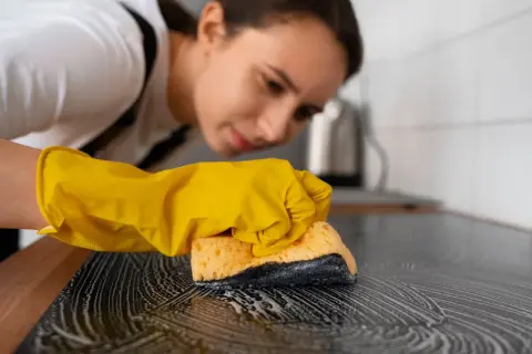 Kobieta w żółtej rękawiczce czyści płytę indukcyjną gąbką z pianą. Dowiedz się, czym czyścić płytę indukcyjną, by lśniła czystością.