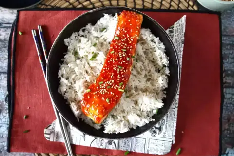 Łosoś w sosie gochujang z sezamem i ryżem, podany z pałeczkami.