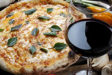 Pizza fumante con basilico e un bicchiere di vino rosso, il perfetto vino per pizza.